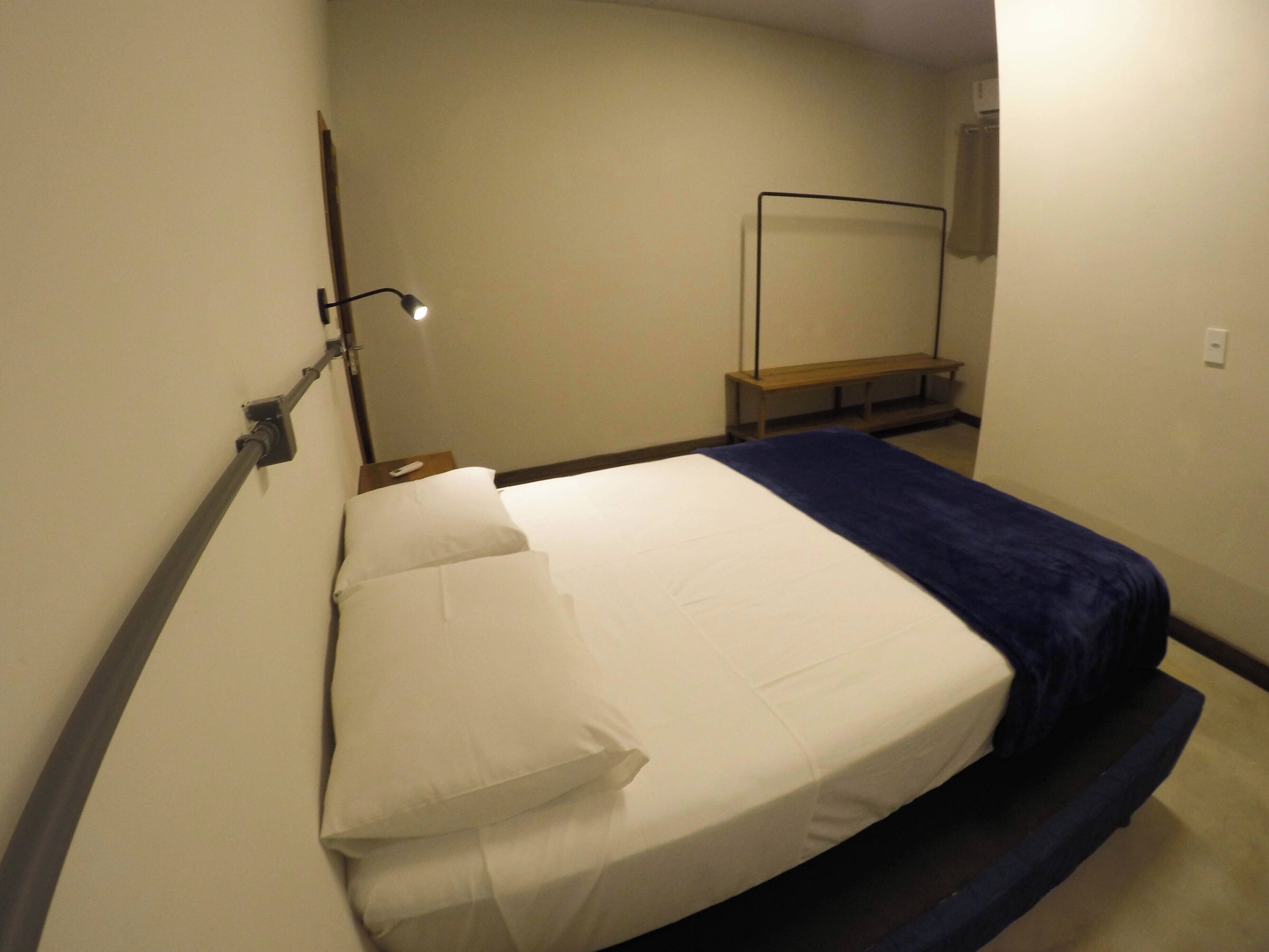 A neatly made bed with white and blue bedding, a bedside lamp, and a wooden bench against the wall.