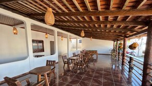 Un comedor amplio con mesas y bancos de madera, suelo de baldosas y lámparas colgantes.