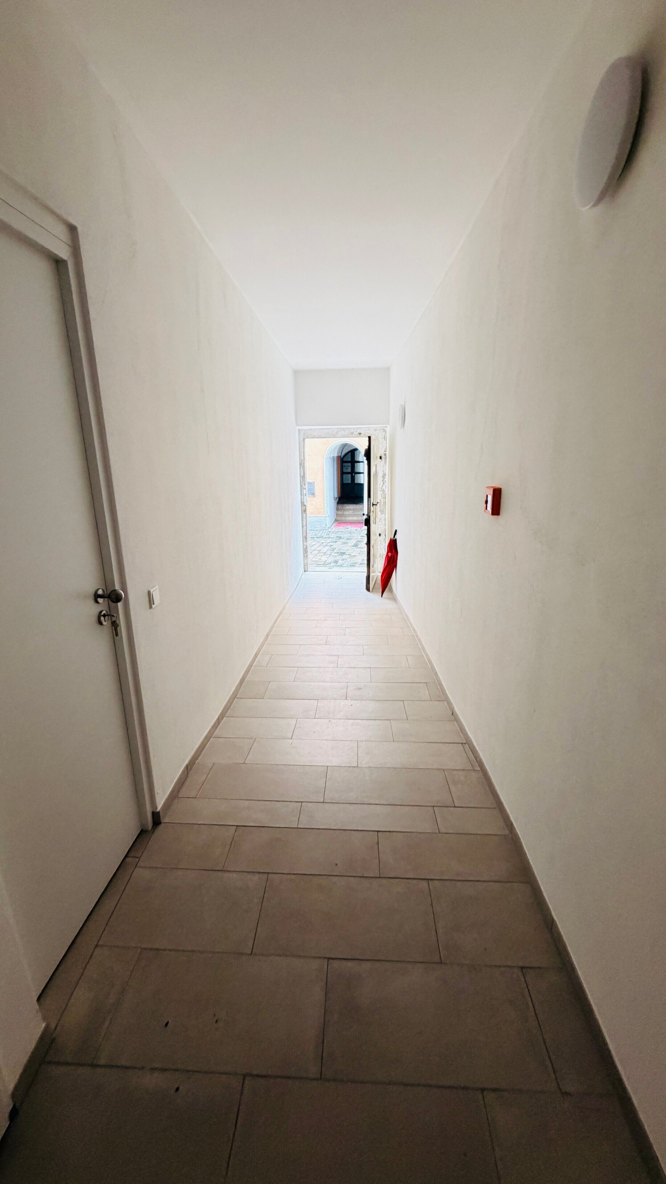 Un couloir étroit, dont le sol est recouvert de carreaux, mène à une porte située au fond.