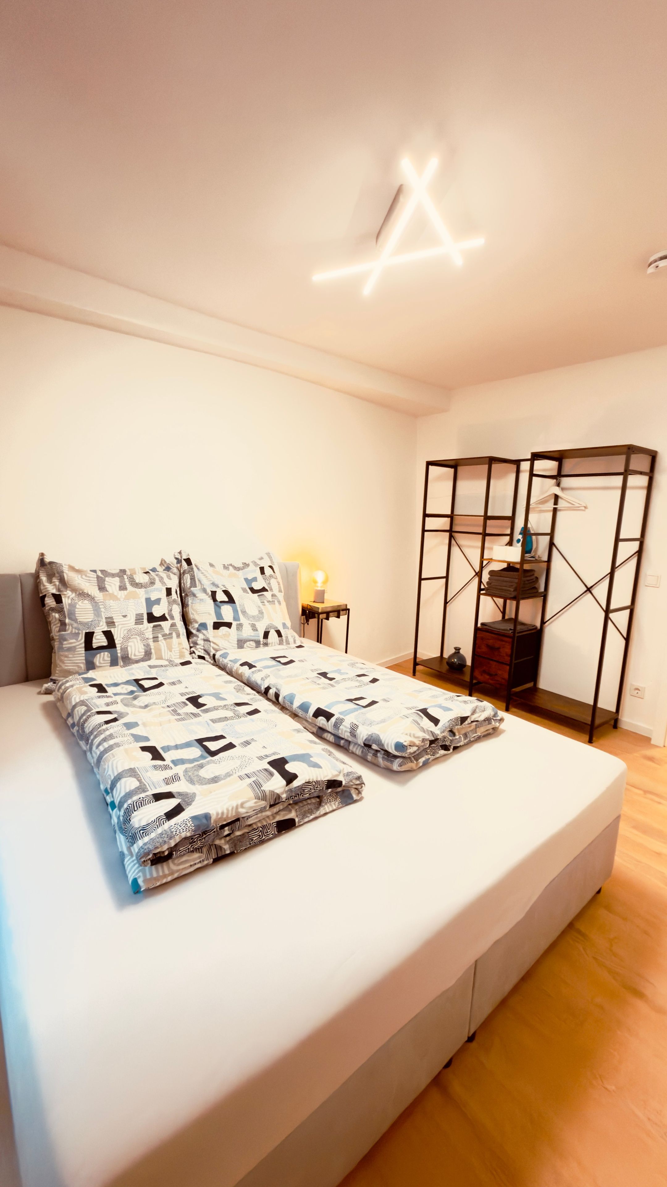 A neatly made bed with patterned bedding, a bedside lamp, and a built-in wardrobe with a mirror.