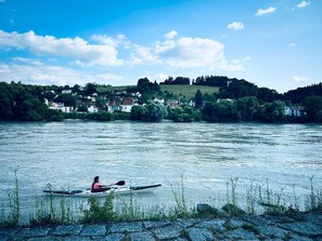 A calm river with a kayaker, houses on the opposite bank, and a clear sky. - The Cozy Corner – Passau (Passau)
