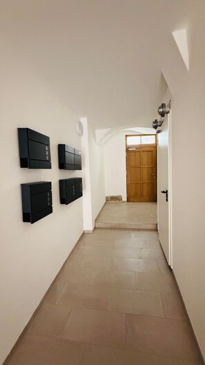 A hallway with a wooden door at the end, white walls, and black mailboxes mounted on the wall. - Cozy Corner – Passau (Passau)