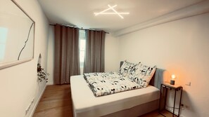 A bedroom with a bed, curtains, a bedside table with a lamp, and a wall-mounted light fixture. - Cozy Corner – Passau (Passau)