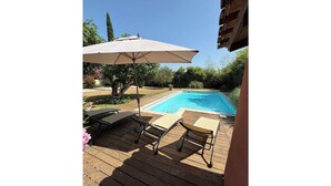 Une terrasse en bois avec deux chaises longues et un grand parasol, donnant sur une piscine.