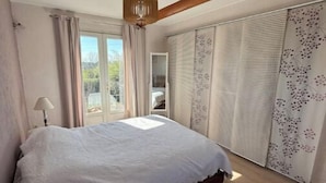 Une chambre avec un grand lit, une petite table ronde, un ventilateur de plafond et une vue par la fenêtre.