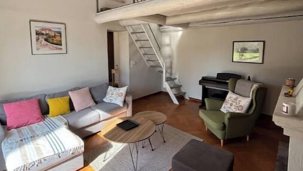 Un vaste espace de vie comprenant un canapé, des fauteuils et une table basse. Un escalier mène à l’étage supérieur.