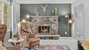 A cozy living room with a stone fireplace, leather armchair, and a bookshelf. - Access to PGA Golf Course- Private Hot Tub-Firepit (Tobyhanna)
