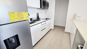 A modern kitchen with white cabinets, a stainless steel refrigerator, a microwave, and a sink. - Modern and cozy apartment in the heart of Panama City, ideal for business travelers and digital nomads. Pool, gym, and coworking space available, with valet parking offered as an optional service. (Panamá)