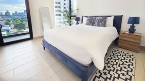 A modern bedroom with a large bed, a view of the city through a balcony, and a patterned rug. - Modern and cozy apartment in the heart of Panama City, ideal for business travelers and digital nomads. Pool, gym, and coworking space available, with valet parking offered as an optional service. (Panamá)