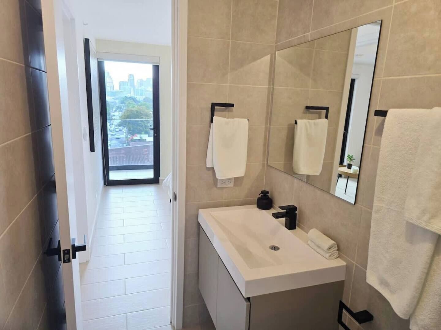 A modern bathroom with a large mirror, white sink, and two towels.