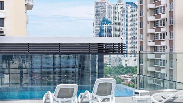 A rooftop pool area with two lounge chairs and a glass railing overlooking a cityscape. - Modern and cozy apartment in the heart of Panama City, ideal for business travelers and digital nomads. Pool, gym, and coworking space available, with valet parking offered as an optional service. (Panamá)