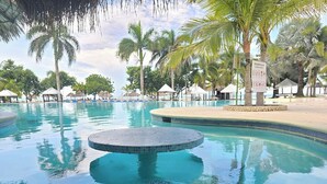 En swimmingpool med ett runt område för bubbelbad, omgiven av palmer och strandparasoller.