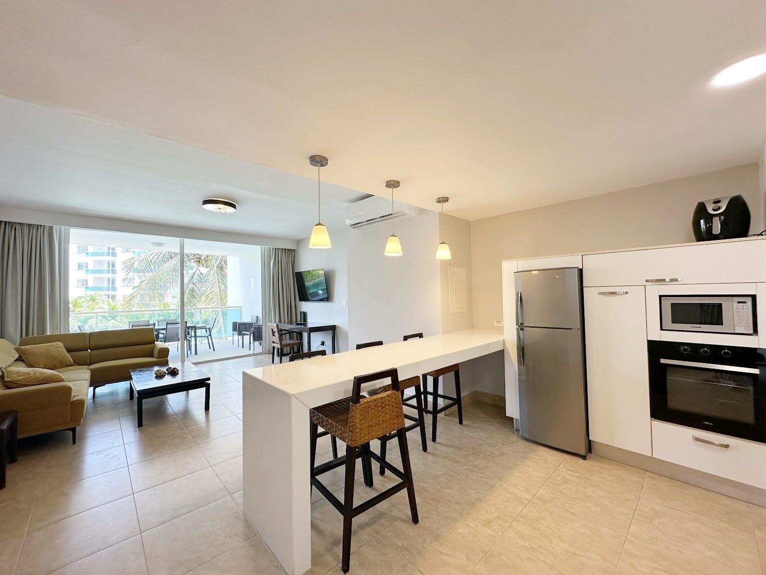 Cozinha moderna com ilha central, sala de jantar com sofá e cadeiras, e sala de estar com uma janela grande.