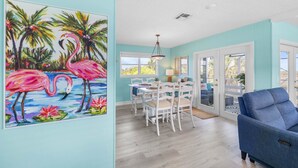 A dining area with a white table and chairs, a blue sofa, and a painting of flamingos on the wall.