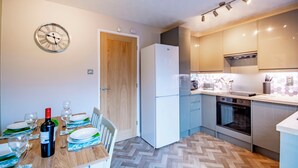 A compact kitchen with a refrigerator, oven, and microwave. There is a dining table with plates and a bottle of wine.
