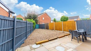 A backyard with a patio area, a table with chairs, and a wooden fence.