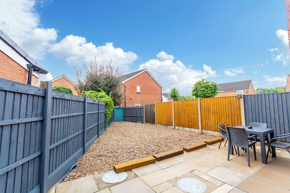 A backyard with a patio area, a table with chairs, and a wooden fence. - Goldcrest House (Nottingham)