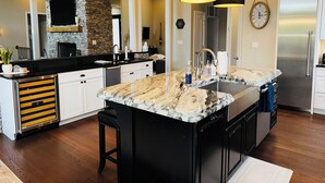 Une cuisine moderne dotée d’un grand îlot central, de meubles de rangement noirs et d’un mur d’accent en pierre.