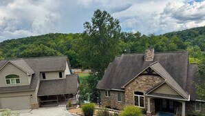 Un quartier résidentiel composé de deux maisons aux façades en pierre et en bois, avec une allée et une colline verdoyante en arrière-plan.