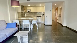 Een moderne woonkamer met een grijze bank, een salontafel en een eethoek met witte stoelen.