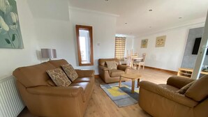 A spacious living room with a brown leather sofa, a coffee table, and a dining area with a table and chairs.