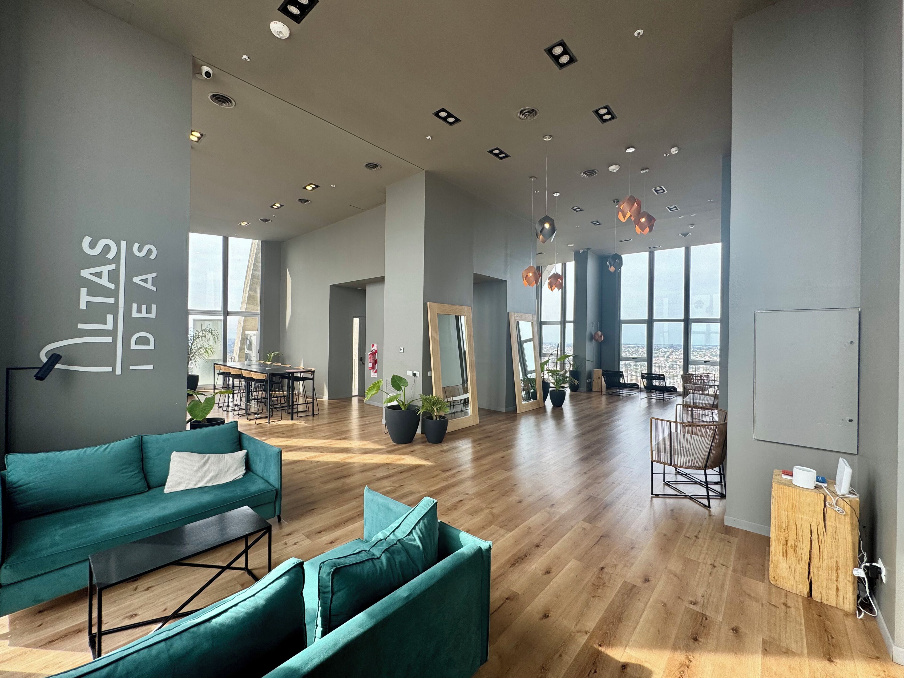 Una oficina amplia con sofás color turquesa, piso de madera y ventanas grandes con vistas a la ciudad.