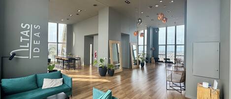 Una oficina amplia con sofás color turquesa, piso de madera y ventanas grandes con vistas a la ciudad.