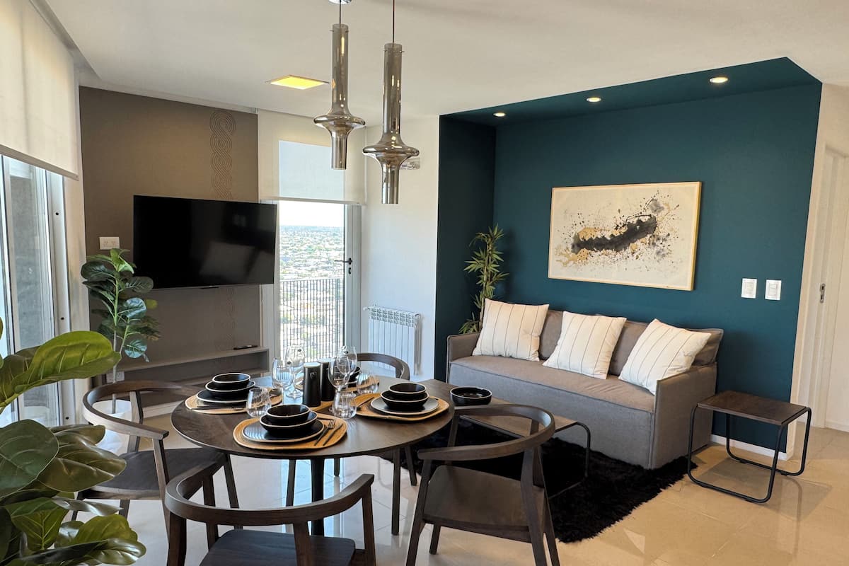 A modern living room with a dining area, a sofa, a TV, and a view of the city.