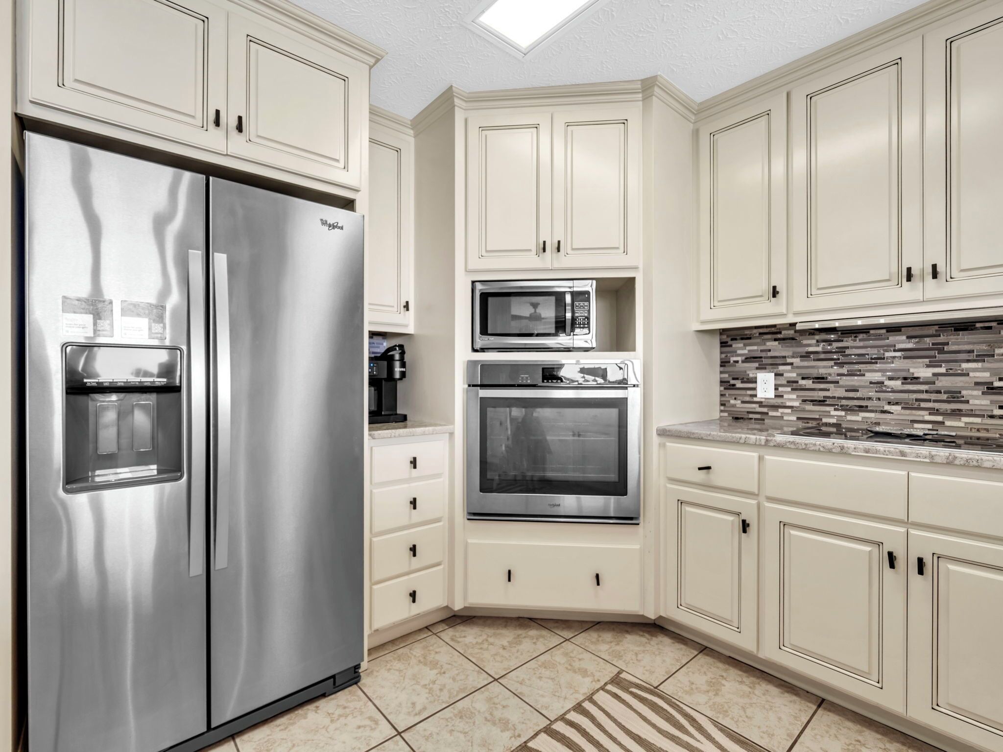 A modern kitchen with stainless steel appliances, white cabinetry, and a tiled backsplash.