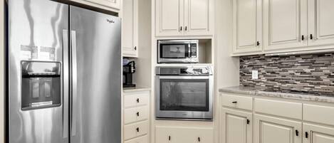 A modern kitchen with stainless steel appliances, white cabinetry, and a tiled backsplash.