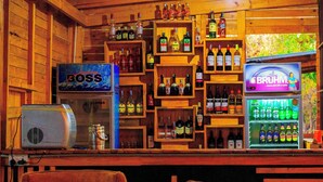 A bar area with shelves of liquor bottles, a 'Boss' sign, a 'Bruhm' sign, and a refrigerator stocked with beverages. - Daga Camp – Bed & Breakfast with a Hunting Edge in Mikumi (Mikumi)