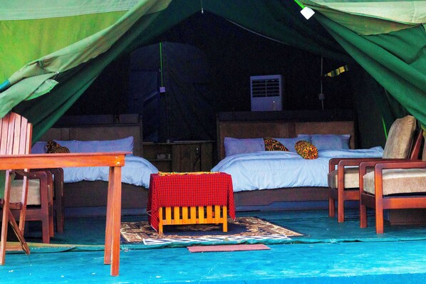 A tented accommodation with two beds, a table, and chairs.