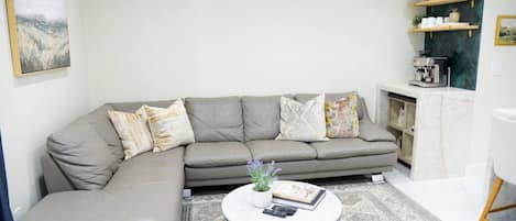 A living room with a grey sectional sofa, a round coffee table, and a patterned rug.