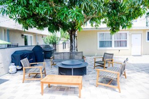Un patio exterior con mobiliario de mimbre, una mesa redonda y una parrilla.