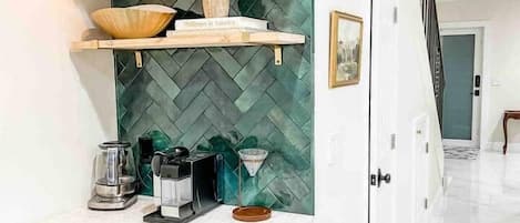 A kitchen with a herringbone-patterned backsplash, wooden shelves with decorative items, a coffee maker, and a built-in oven.