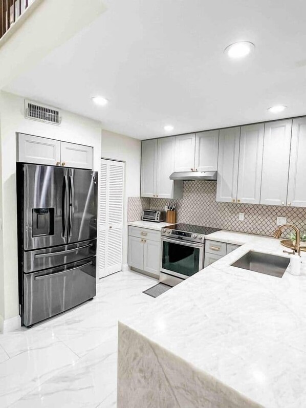 A modern kitchen with stainless steel appliances, white cabinetry, and a marble countertop.