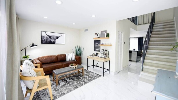 A modern living room with a brown leather sofa, a coffee table, and a desk with a computer. - The Hamptons Hideaway (Hollywood)