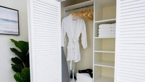 A walk-in closet with a white interior, a hanging rack with clothes, and a shelf with folded items. - The Hamptons Hideaway (Hollywood)