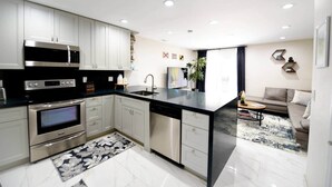 A modern kitchen with stainless steel appliances, white cabinetry, and a black countertop. - The Hamptons Hideaway (Hollywood)