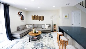 A modern living room with a grey sectional sofa, a round coffee table, and a black floor lamp. - The Hamptons Hideaway (Hollywood)