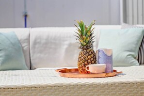 Un sofá de mimbre con una piña y una taza estampada sobre una bandeja.