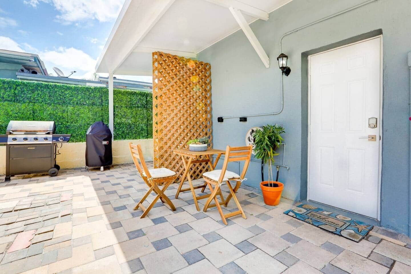 Un patio al aire libre con una parrilla, sillas plegables, una mesa y una planta en maceta.