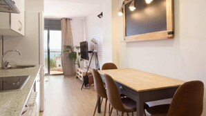 Une cuisine moderne avec une table et des chaises en bois, un téléviseur posé sur un trépied et un tableau noir accroché au mur.