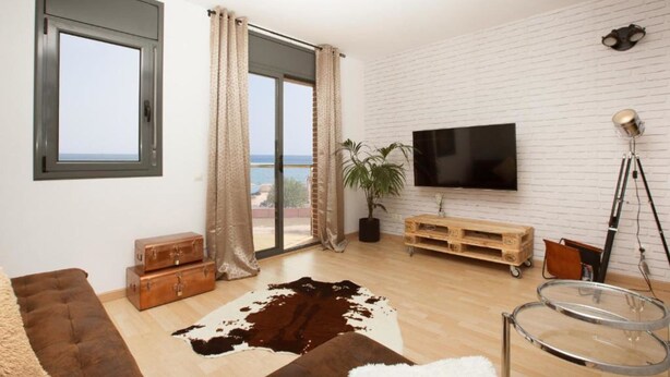 Un salon moderne doté d’un grand téléviseur, d’un parquet en bois, d’un tapis en peau de vache et offrant une vue sur la mer grâce à une porte coulissante.
