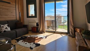 Un salon moderne comprenant un canapé, une table basse, une cheminée et une grande porte-fenêtre coulissante donnant sur un balcon avec vue sur des immeubles et un plan d’eau.