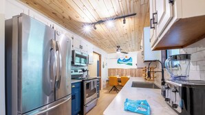 A modern kitchen with stainless steel appliances, wooden ceiling, and a central island.