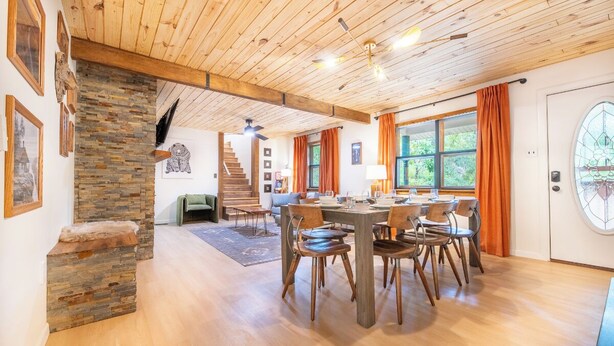 A spacious dining area with a wooden table and chairs, a stone fireplace, and a staircase leading to another level.