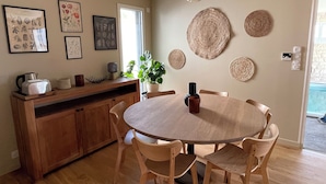 A dining area with a round wooden table, six wooden chairs, a wooden buffet, and wall-mounted woven decorations. - Gîte Ondine - House with indoor pool (Belz)