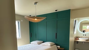 A bedroom with a bed, a hanging light fixture, a teal accent wall, and a bathroom with a mirror and sink. - Gîte Ondine - House with indoor pool (Belz)