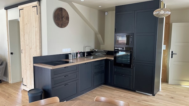 A modern kitchen with dark cabinetry, a wooden countertop, and a built-in oven. - Gîte Ondine - House with indoor pool (Belz)